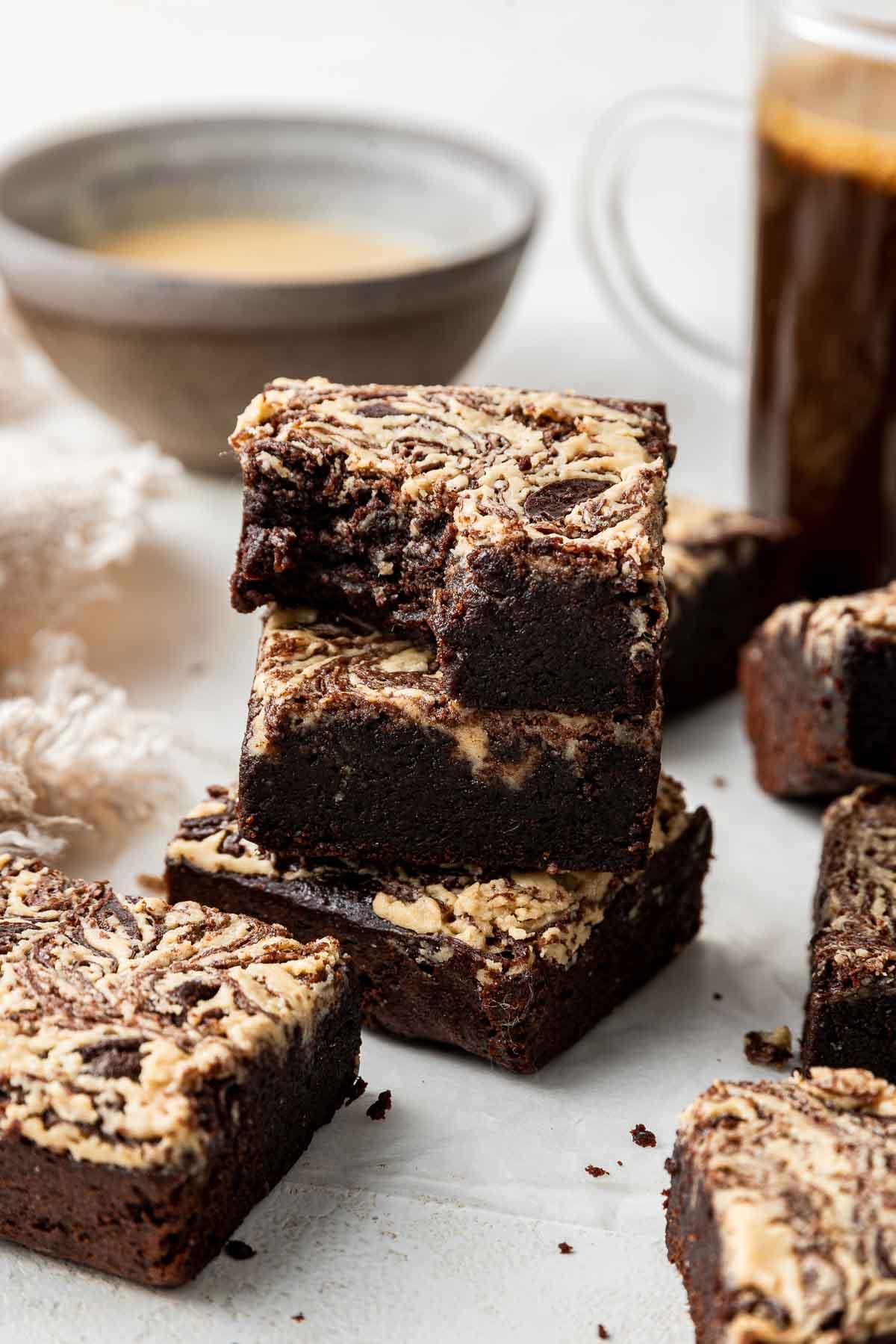 Pila di brownies al tahini con un morso mancante e caffè sullo sfondo.