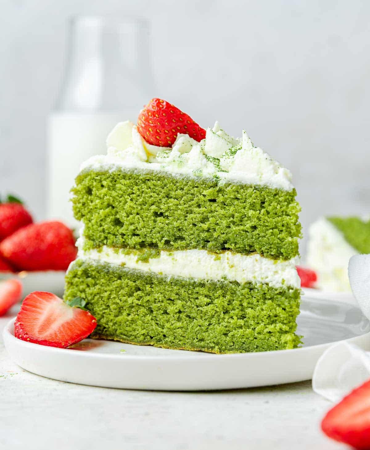 Torta al Matcha 2 Torta al Matcha di un verde brillante con glassa bianca e fragole fresche, scatto verticale ravvicinato.