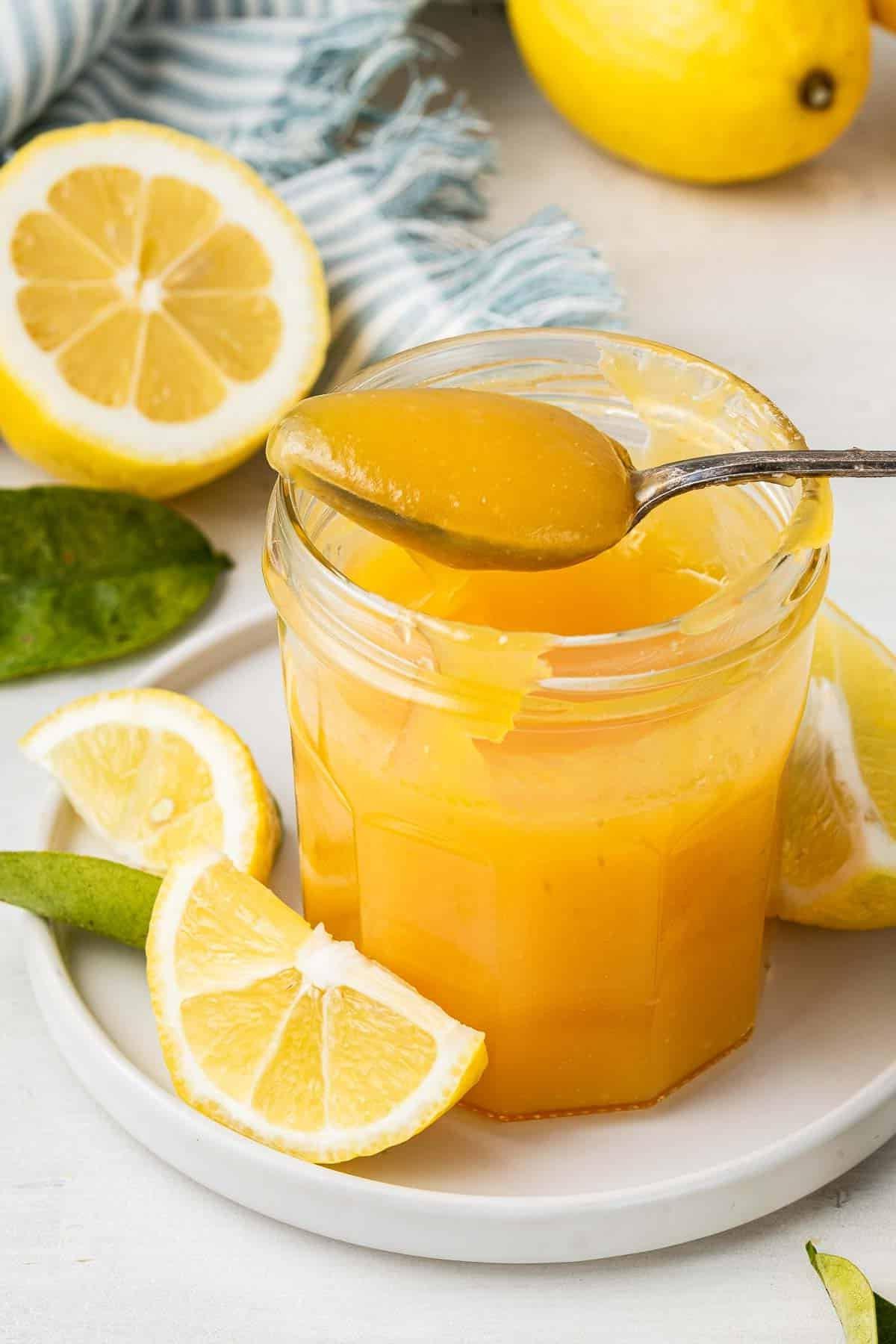 **Lemon Curd al Microonde in Piccola Quantità** 2 Barattolo di vetro di crema al limone al microonde con un cucchiaio che rimuove una porzione.