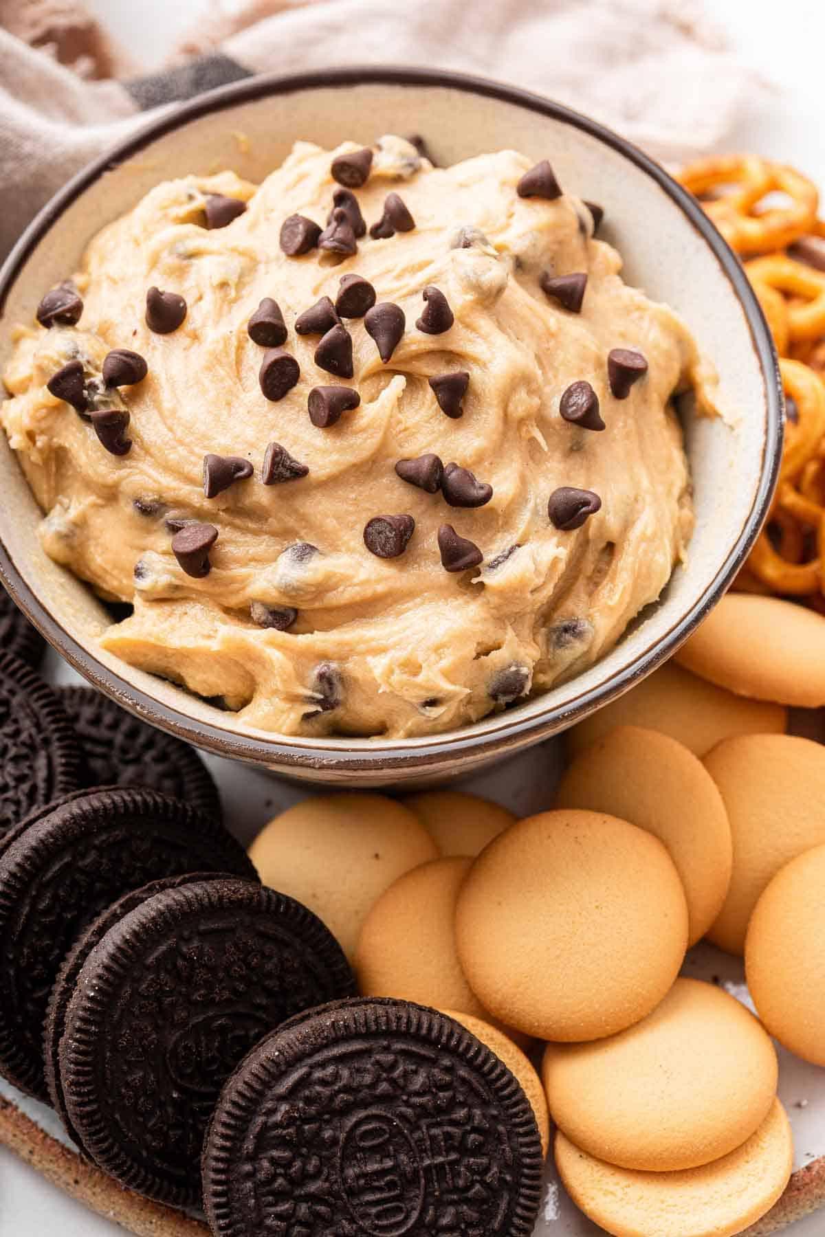 **Crema Impasto Biscotti Monoporzione** 2 Ciotola bianca con dip di impasto per biscotti al cioccolato circondata da biscotti e wafer croccanti.