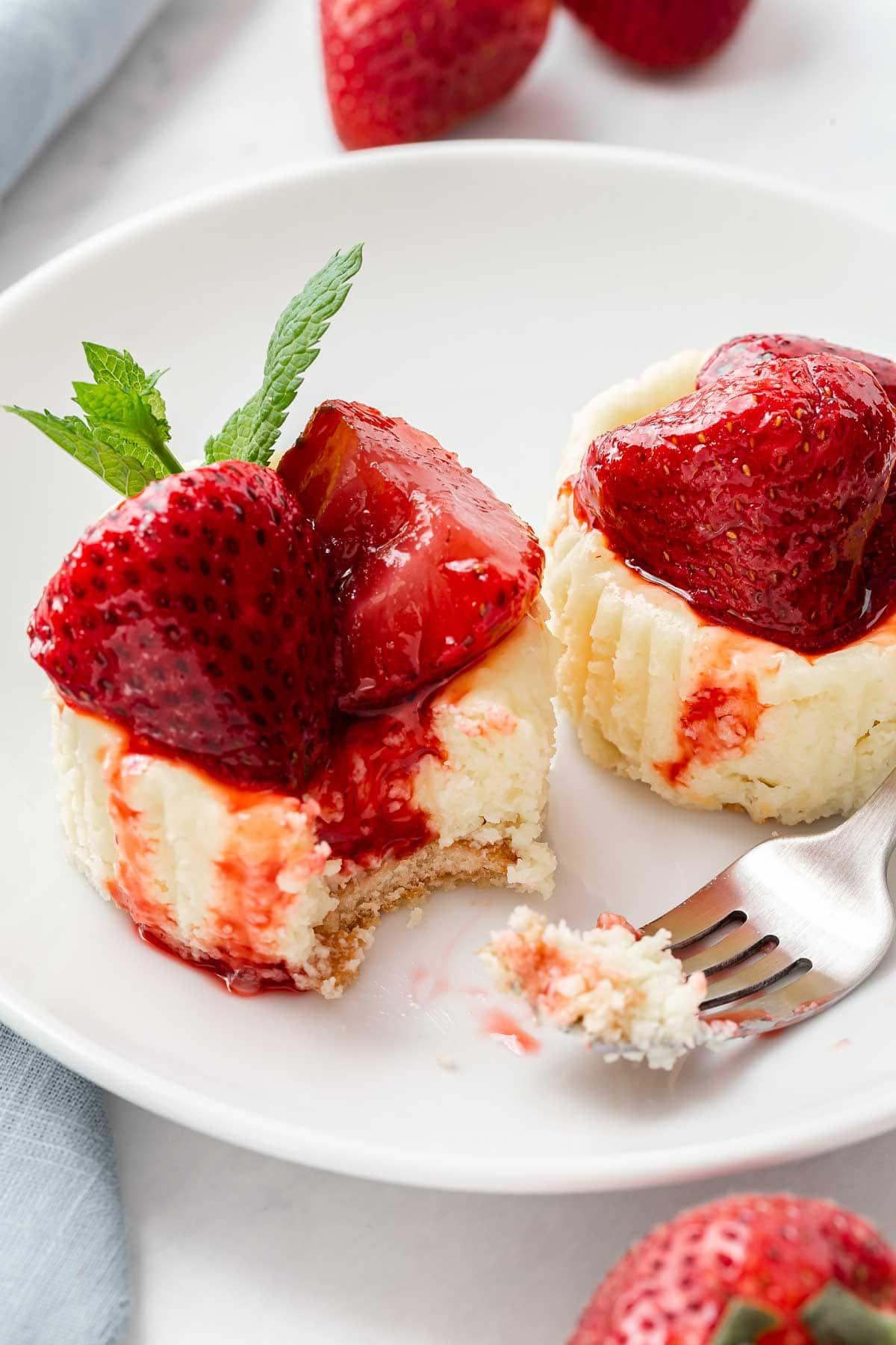 Due mini cheesecake alle fragole su un piatto con una forchetta.