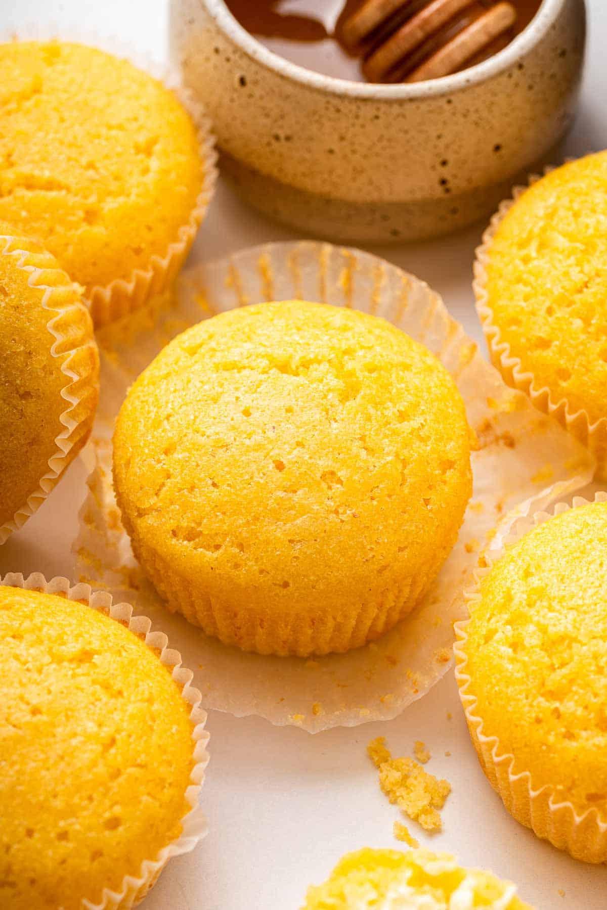 Ricetta Muffin al Mais 2 Sei muffin di mais gialli su un bancone accanto a un vasetto di miele.