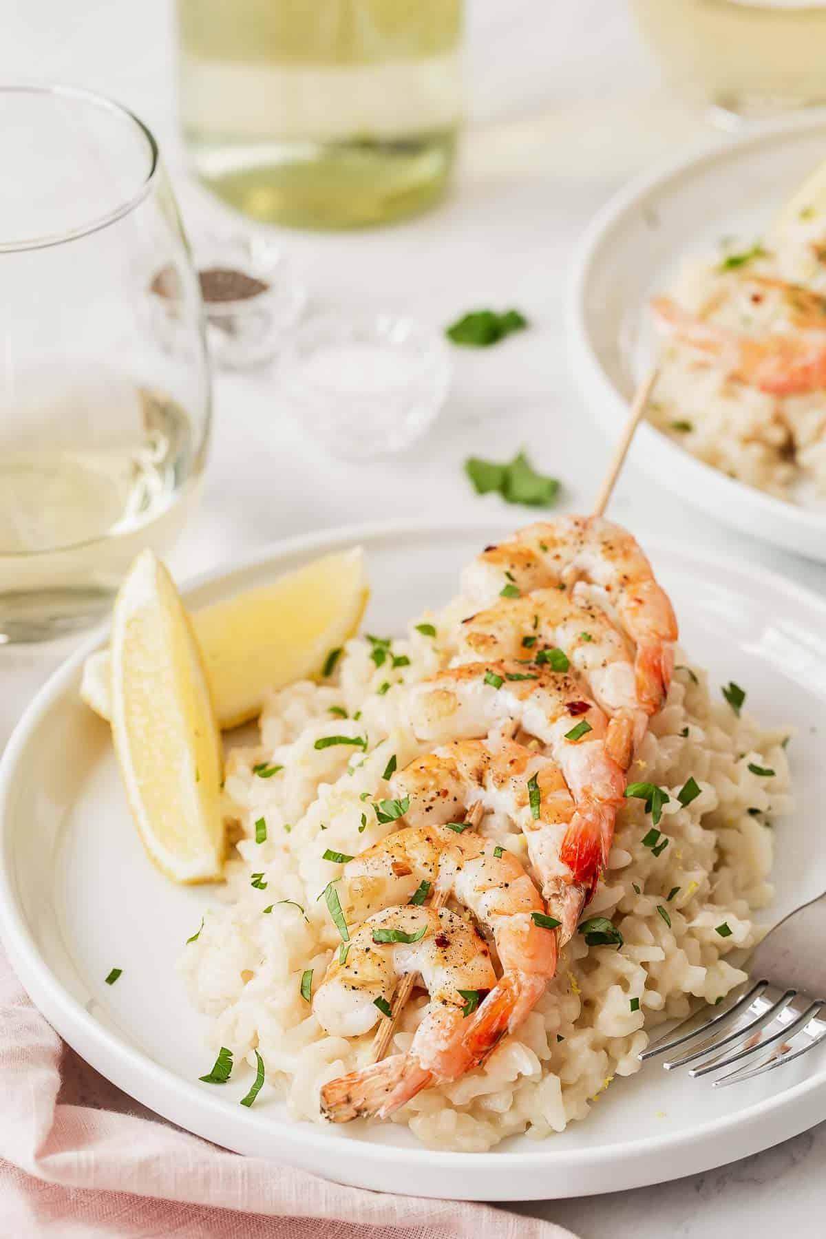 Gamberi su spiedini serviti su risotto al limone con spicchi di limone.