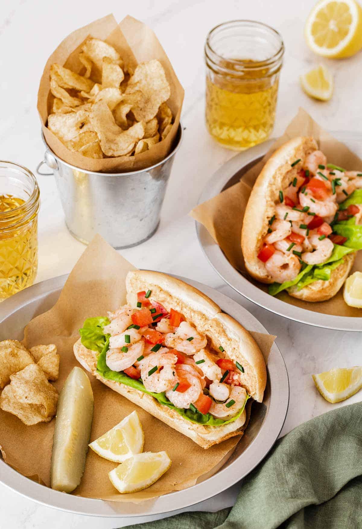 Panini Po' Boy di gamberi su piatti con patatine e sottaceti.