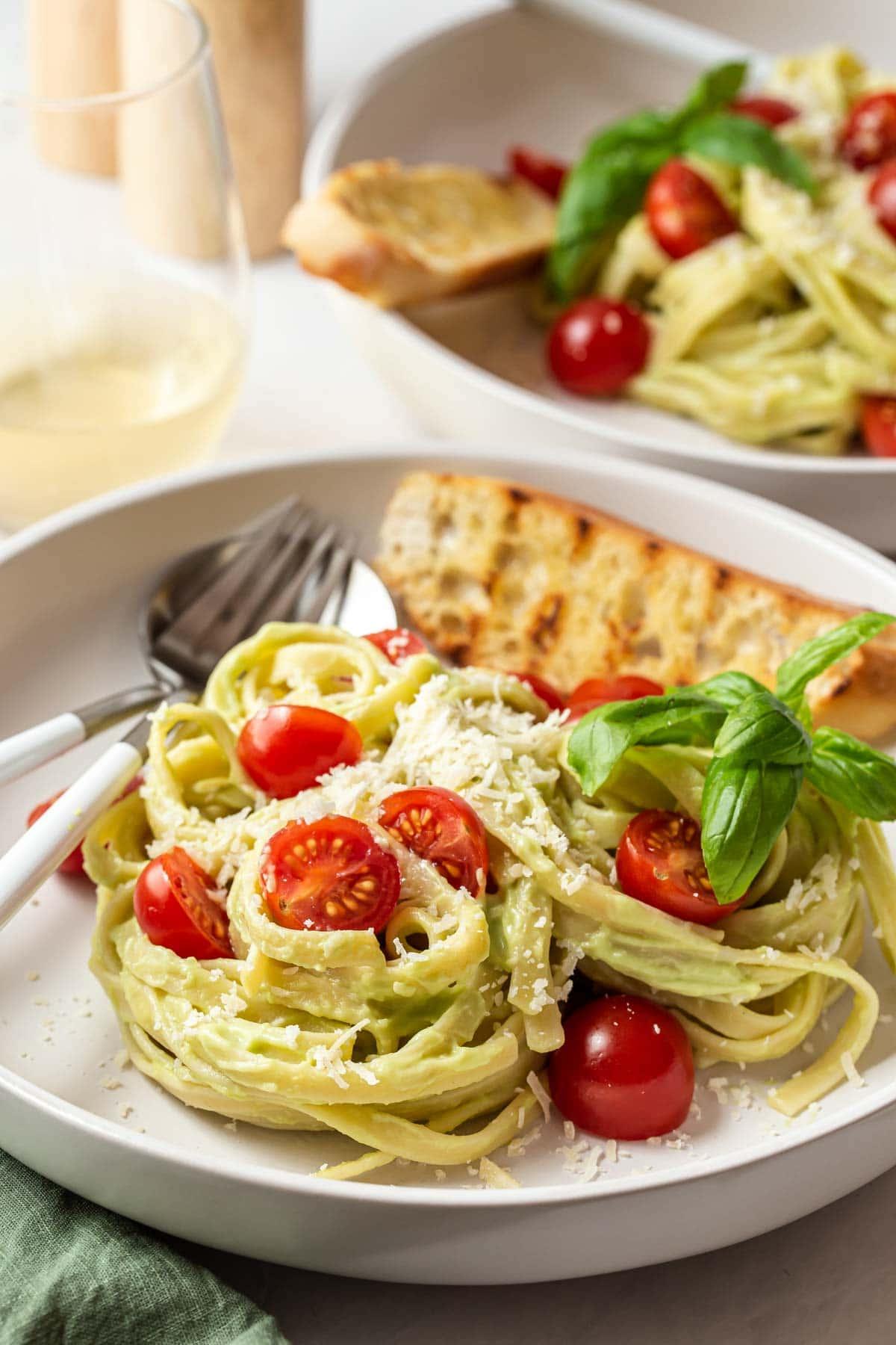Avocado pasta with tomatoes and grilled bread on plates.