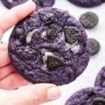 Mano che tiene un biscotto all'ube con pezzetti di Oreo sbriciolati all'interno.