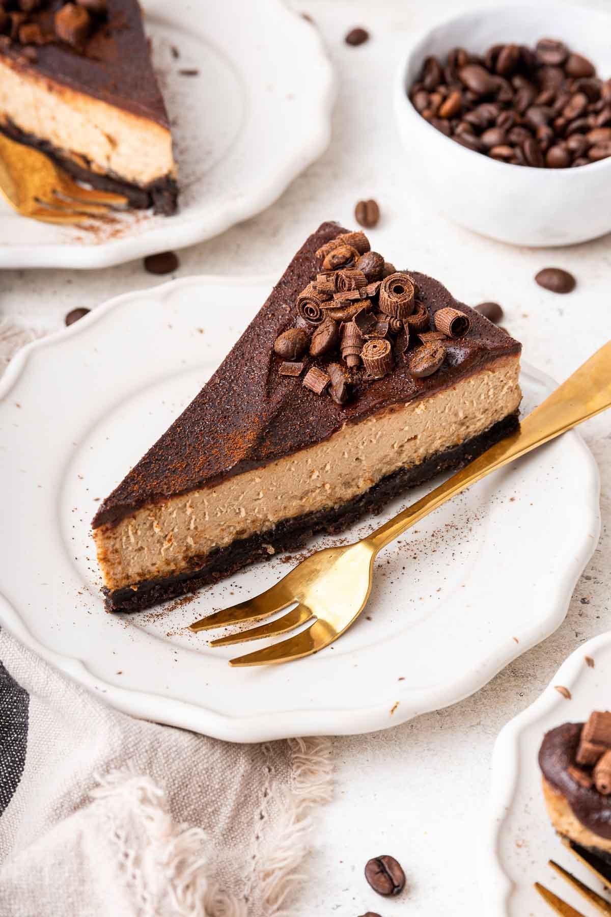 Cheesecake al caffè 11 Fetta di cheesecake al caffè con ganache al cioccolato e forchetta dorata a lato, pronta per essere gustata.