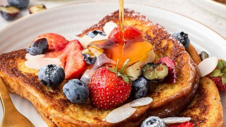 Ricetta del Pain Doré alla Brioche Fatto in Casa (Facile!) 7 French toast di brioche per due su un piatto con frutti di bosco freschi e sciroppo versato sopra.