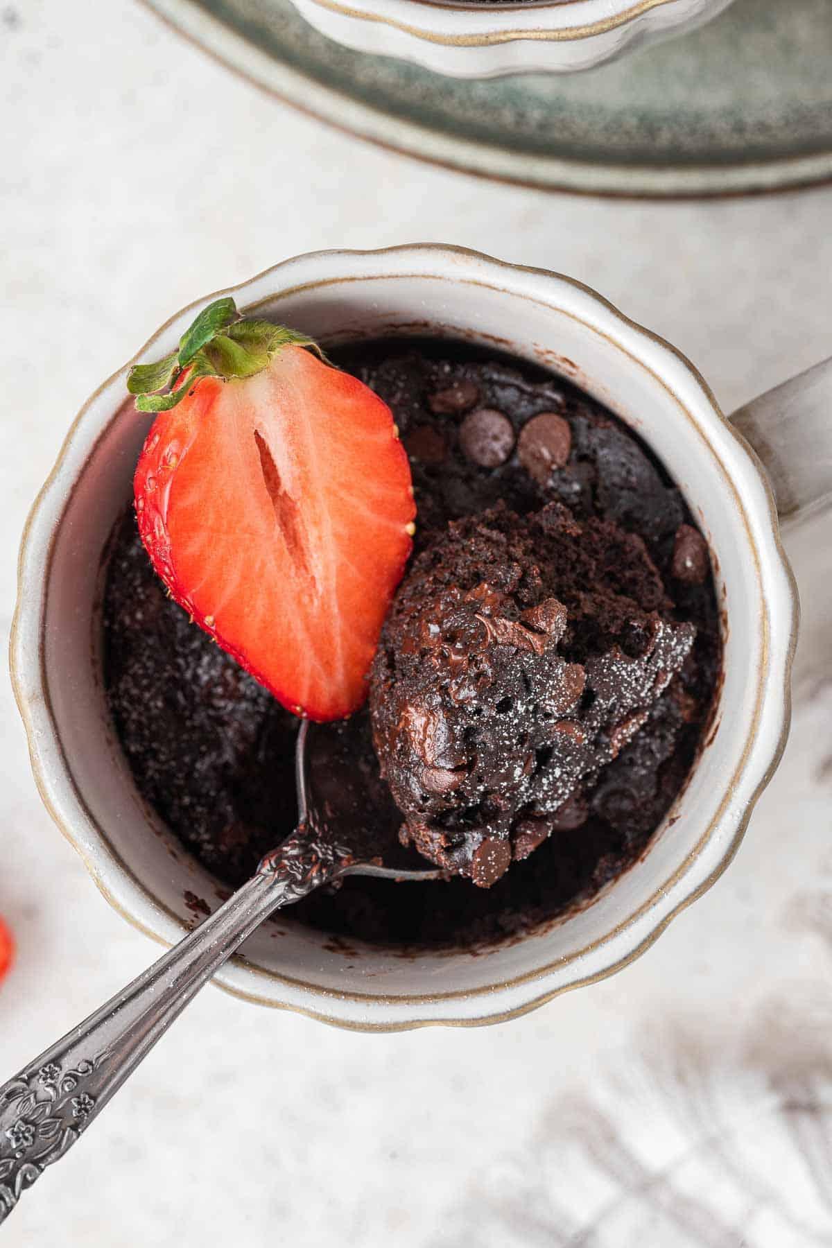 Ricetta Torta al Cioccolato in Tazza 11 Primo piano di torta al cioccolato in tazza con un morso su un cucchiaio e una fragola in cima.