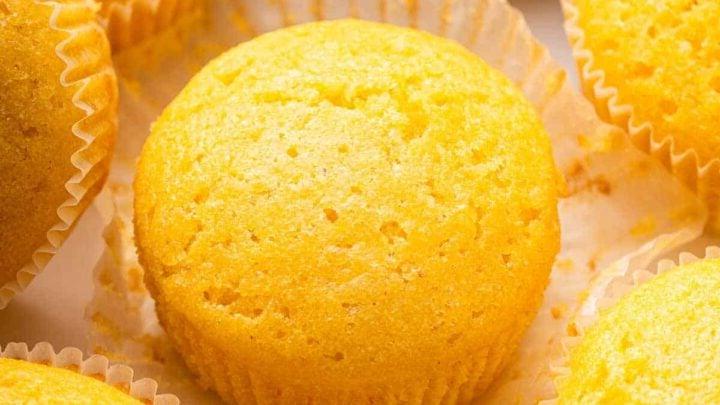 Ricetta Muffin al Mais 11 Sei muffin di mais gialli su un bancone accanto a un vasetto di miele.