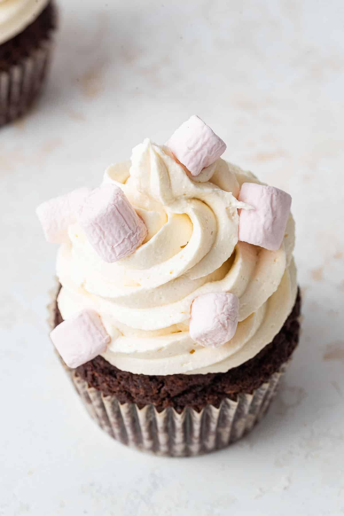Brown cupcake, white frosting, decorated with pink and white baubles.