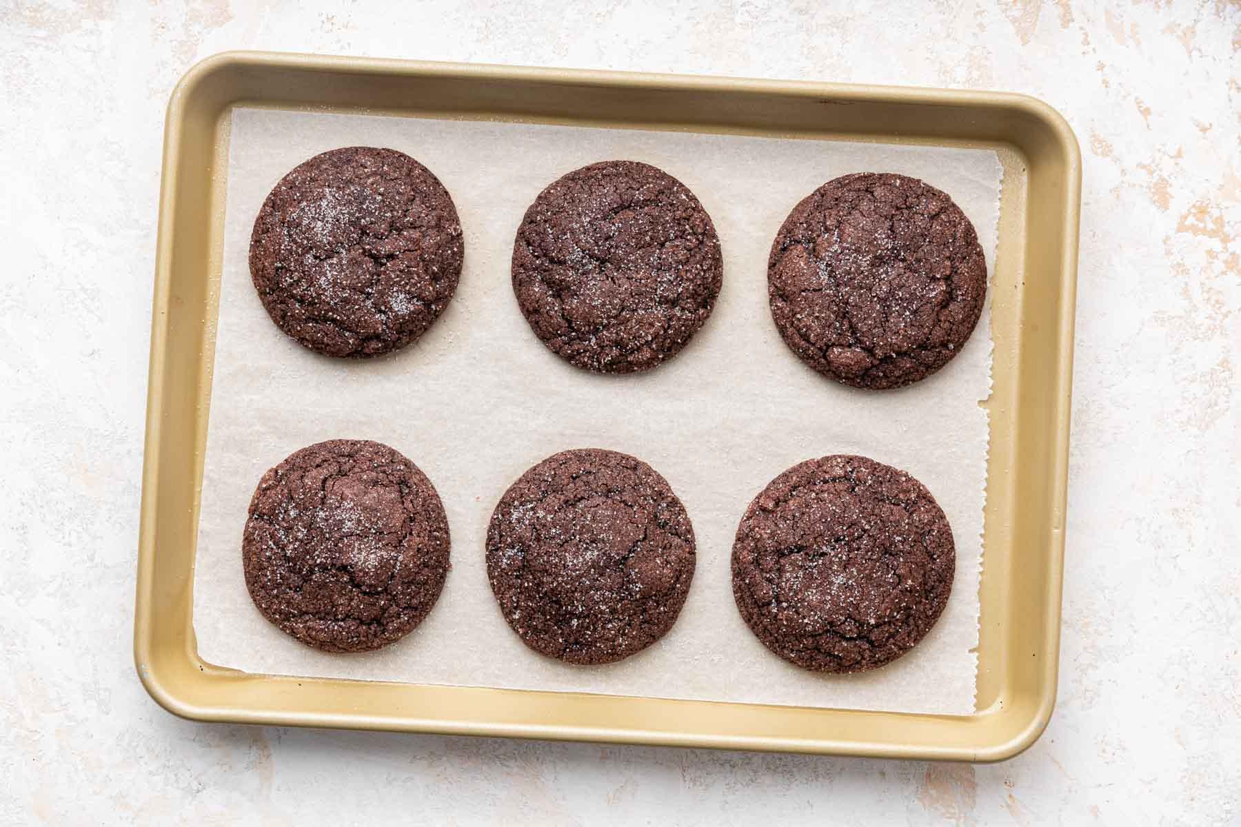 Six brown chocolate sugar cookies on a small cookie sheet.