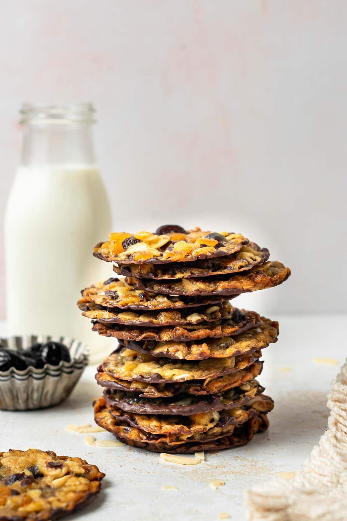 Pila di biscotti sottili con un bicchiere di latte sullo sfondo.
