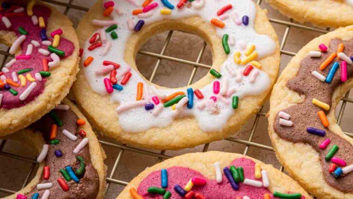 Biscotti Ciambella 15 Donut cookies with pink, white and brown frosting and sprinkles on a wire rack.