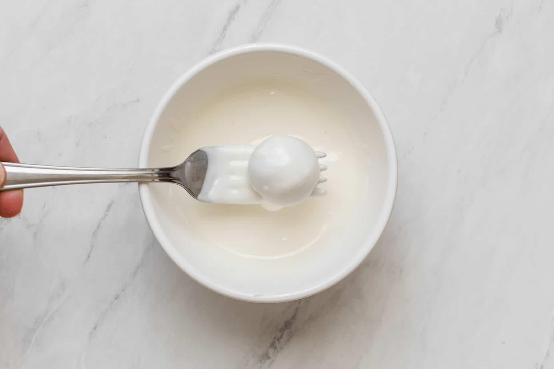 Immersione di tartufi nel cioccolato bianco fuso con una forchetta.