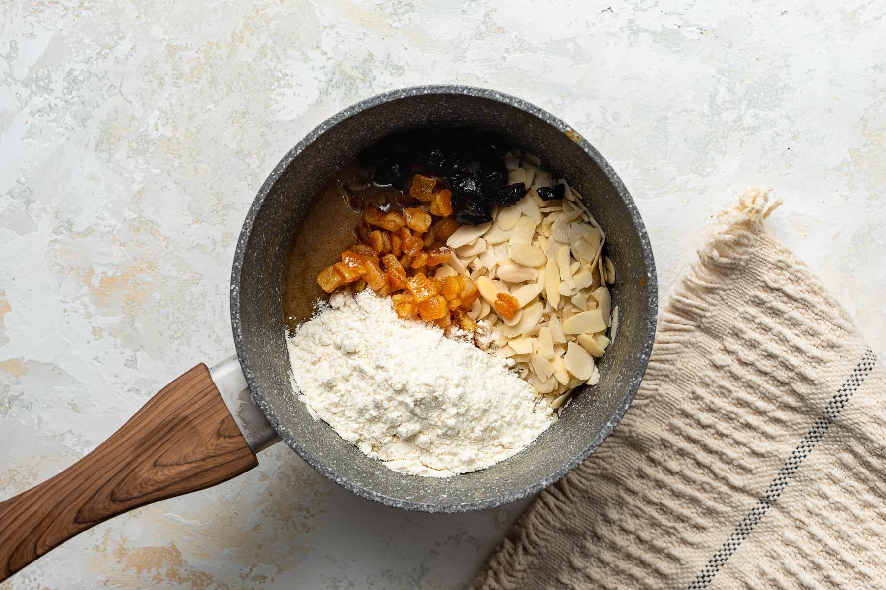 Farina, noci e frutta candita in un pentolino.
