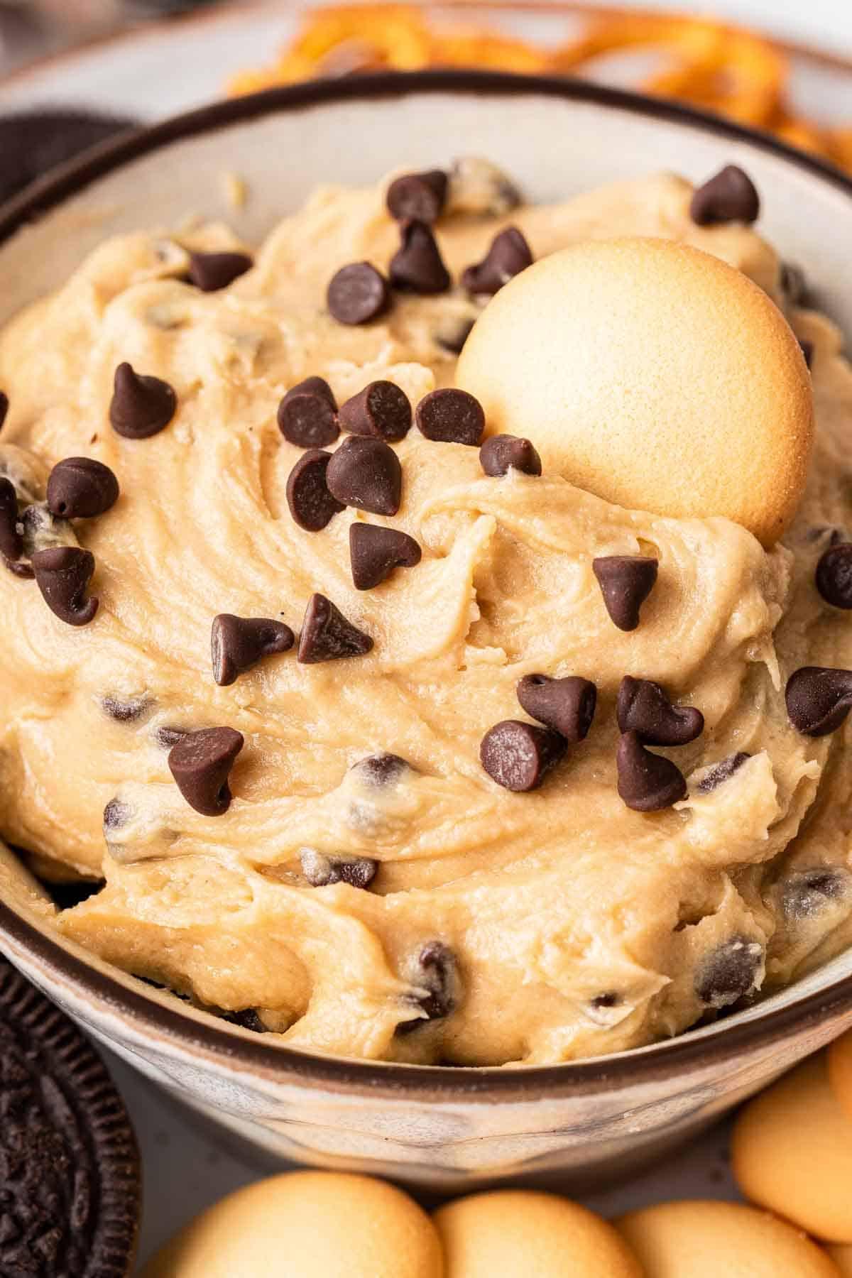 **Crema Impasto Biscotti Monoporzione** 3 Primo piano di dip di impasto per biscotti in una ciotola con un wafer alla vaniglia posato sopra.
