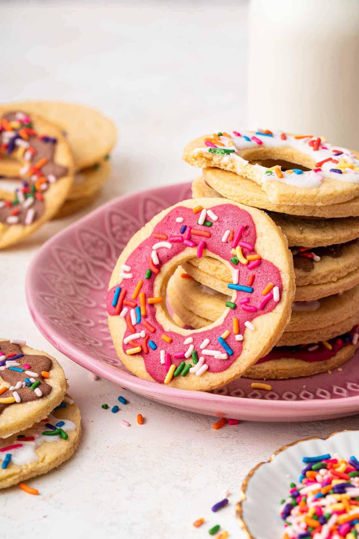 Biscotti Ciambella 3 Donut cookies stacked on a pink plate with milk behind it.