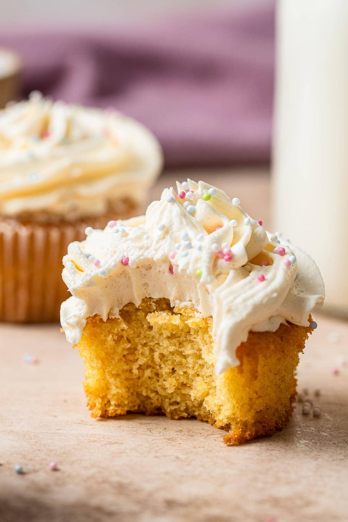 Piccolo Lotto di Cupcakes alla Vaniglia 3 Un cupcake con un morso mancante, che mostra la consistenza interna soffice e la glassa cremosa.