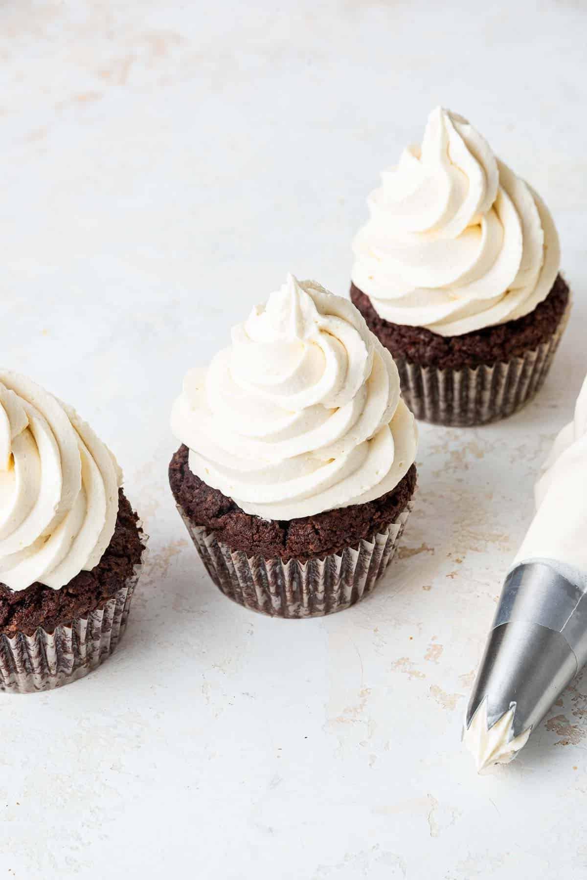 Group of 3 cupcakes with swirled buttercream on top and pastry bag on side.