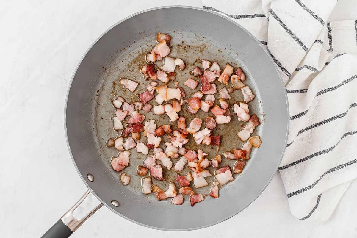 Pezzi di pancetta che cuociono in una padella grigia