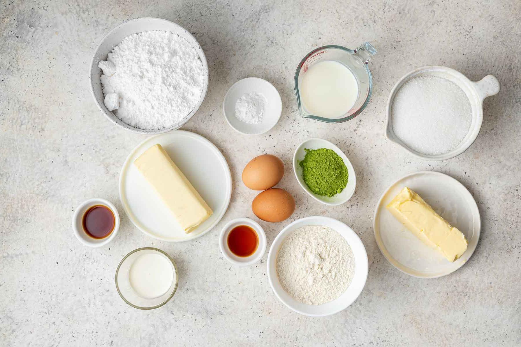 Torta al Matcha 4 Piccole ciotole con ingredienti per la torta, inclusi farina, burro, uova, zucchero e vaniglia.