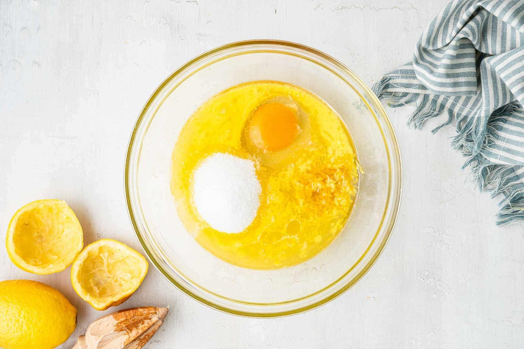 **Lemon Curd al Microonde in Piccola Quantità** 4 Ciotola trasparente con burro fuso, succo di limone, uovo e zucchero sul bancone.