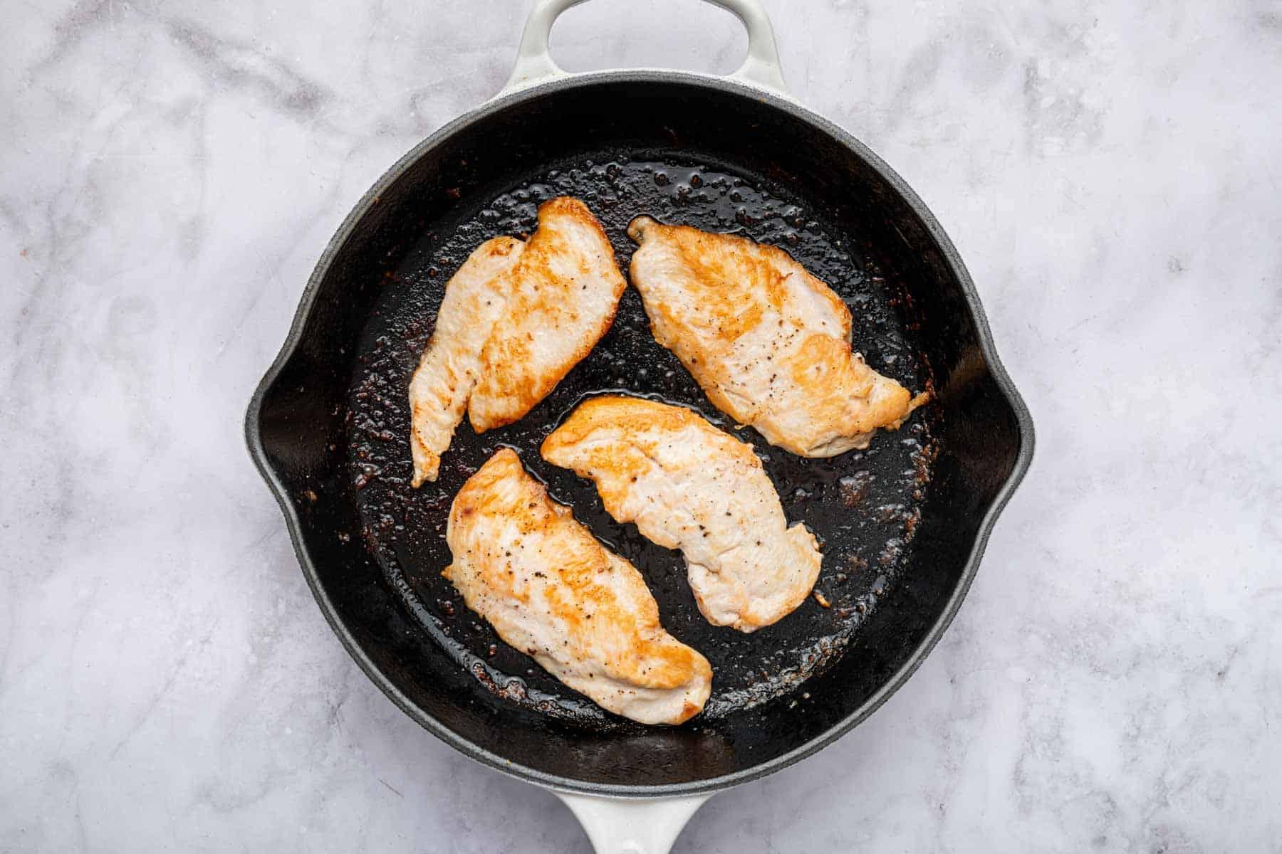 Ricetta del Pollo alla Cipolla Francese 4 Quattro sottili fettine di pollo in una padella di ghisa nera.