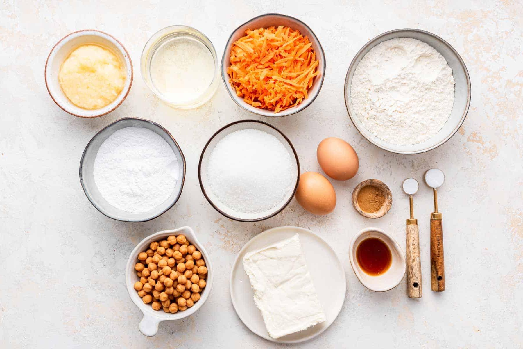 **Tortina di Carote con Glassa al Formaggio Cremoso al Caramello** 4 Piccole ciotole di ingredienti per la cottura disposte su un bancone di marmo, pronte per la preparazione.