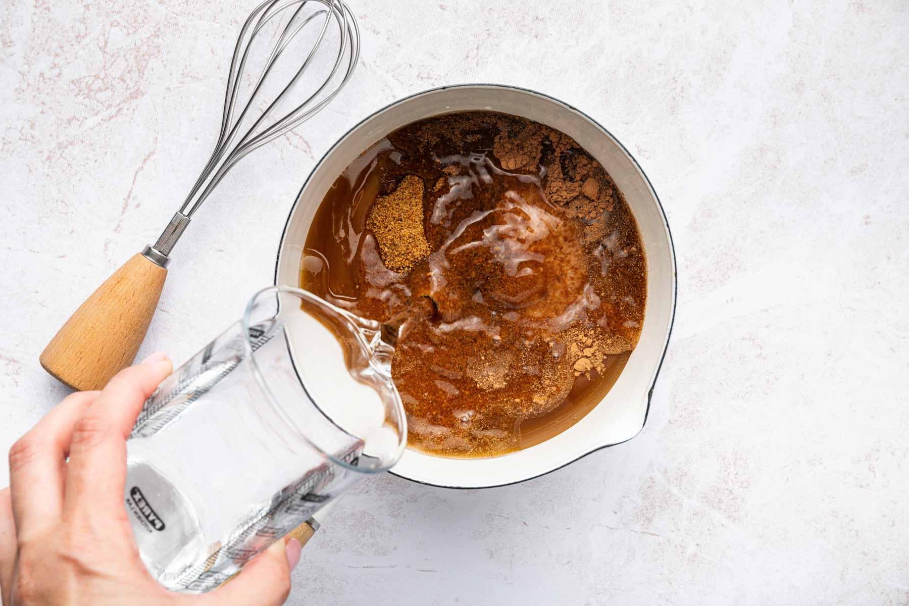 Ricetta Mocaccino Ghiacciato 4 Mano che versa acqua in un pentolino con cacao in polvere e miele.