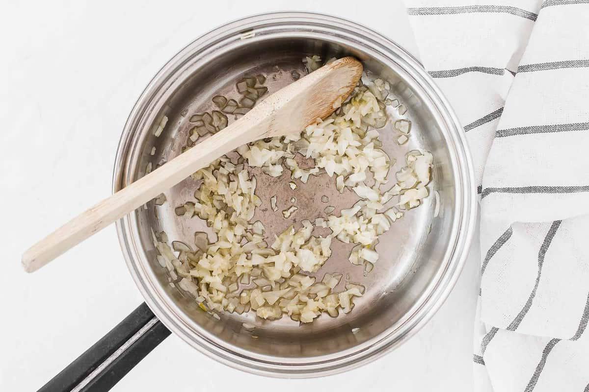 Cipolla e aglio che soffriggono in una padella con un cucchiaio di legno.