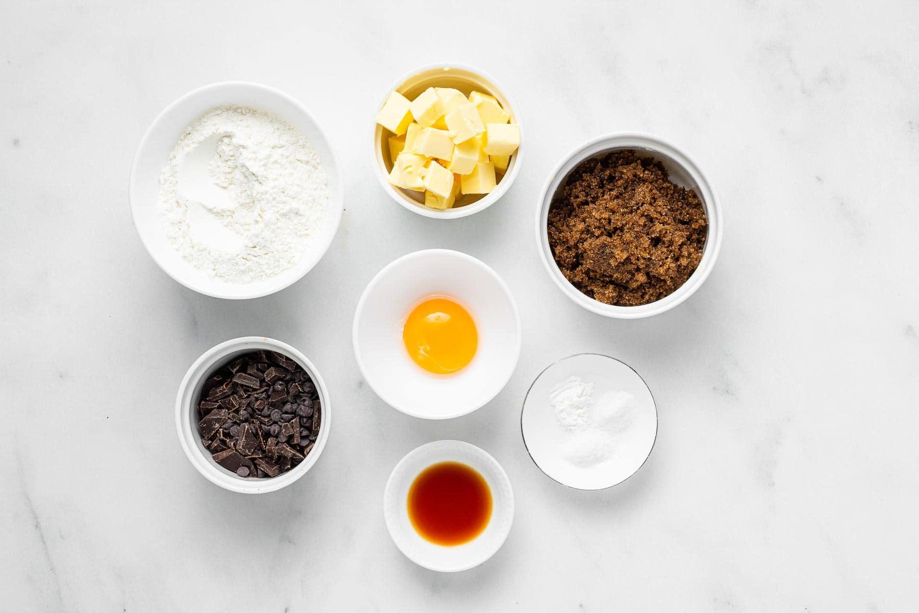 Ingredienti per biscotti al cioccolato con zucchero di canna su tavolo bianco in ciotole.