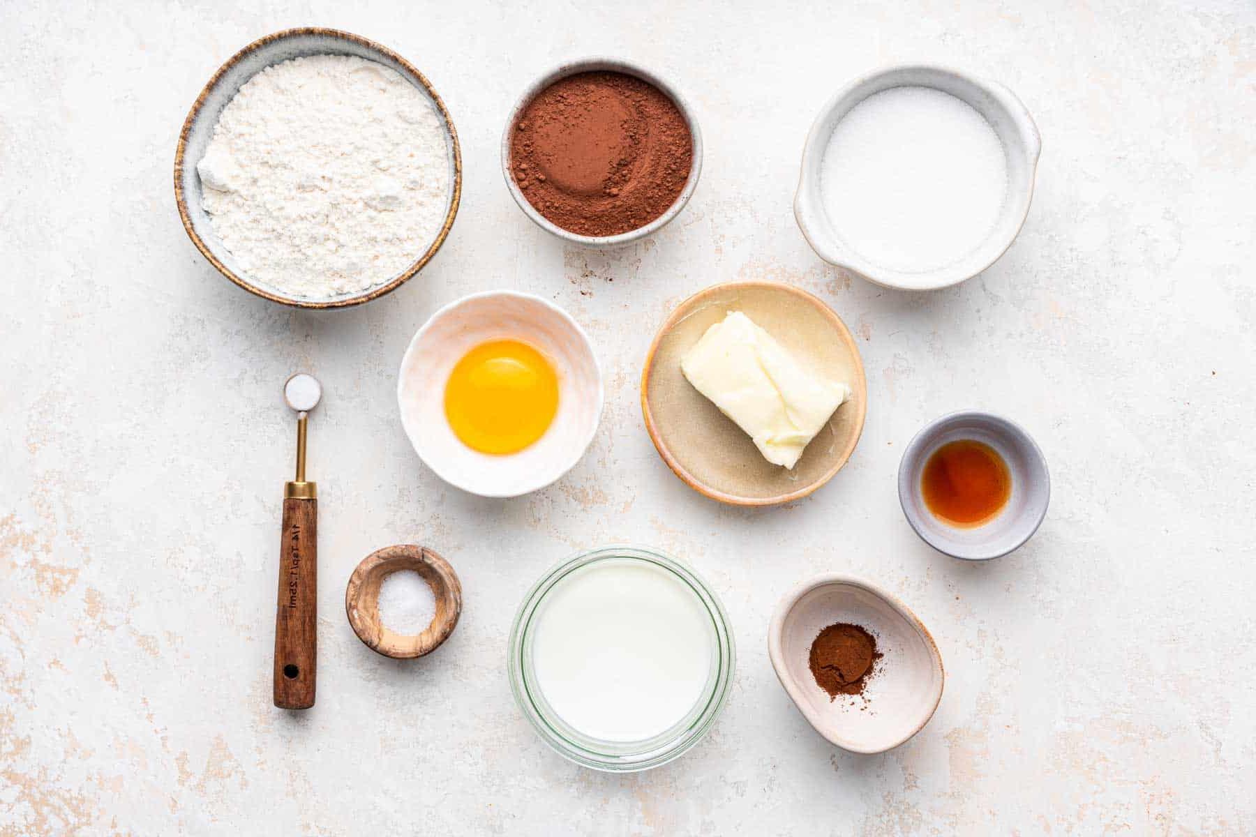 Small bowls of ingredients, including egg, cocoa powder, flour, and sugar on kitchen counter.