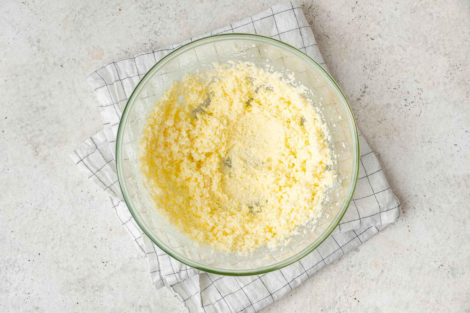 Torta al Matcha 5 Burro giallo brillante e zucchero semolato montati insieme in una ciotola di vetro trasparente.