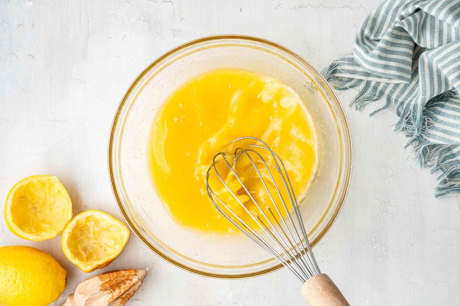 **Lemon Curd al Microonde in Piccola Quantità** 5 Frusta in una ciotola con liquido giallo e bucce di limone a lato.