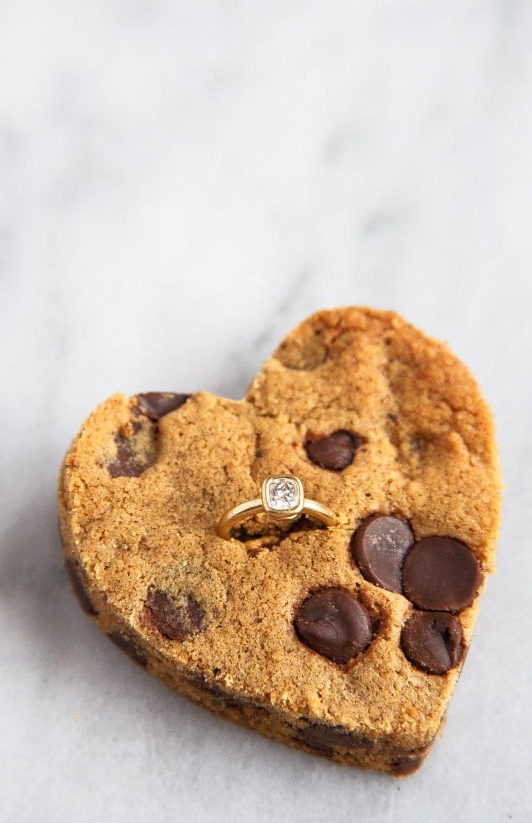 Biscotto con gocce di cioccolato tagliato a forma di cuore con anello di diamanti inserito.