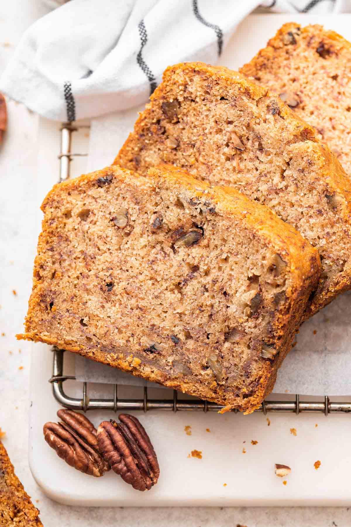 Pane alle banane senza uova 5 Tre fette di banana bread senza uova con noci pecan a lato.
