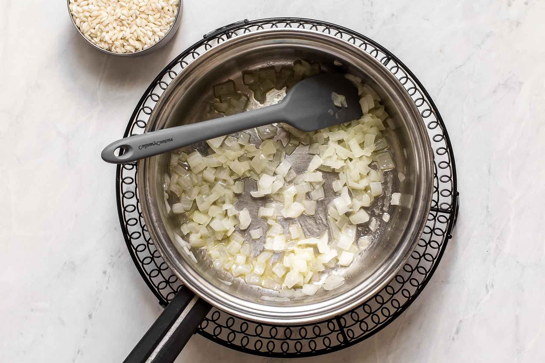 Cipolle che cuociono in una padella d'argento con una spatola.