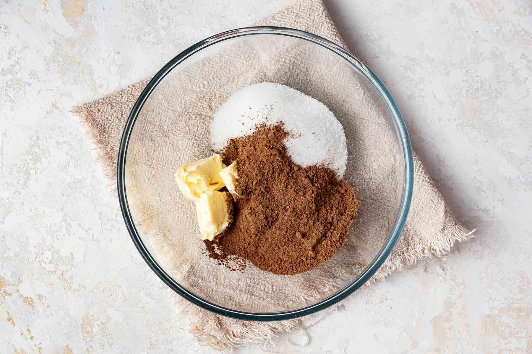 Ciotola trasparente con burro, zucchero e cacao in polvere.