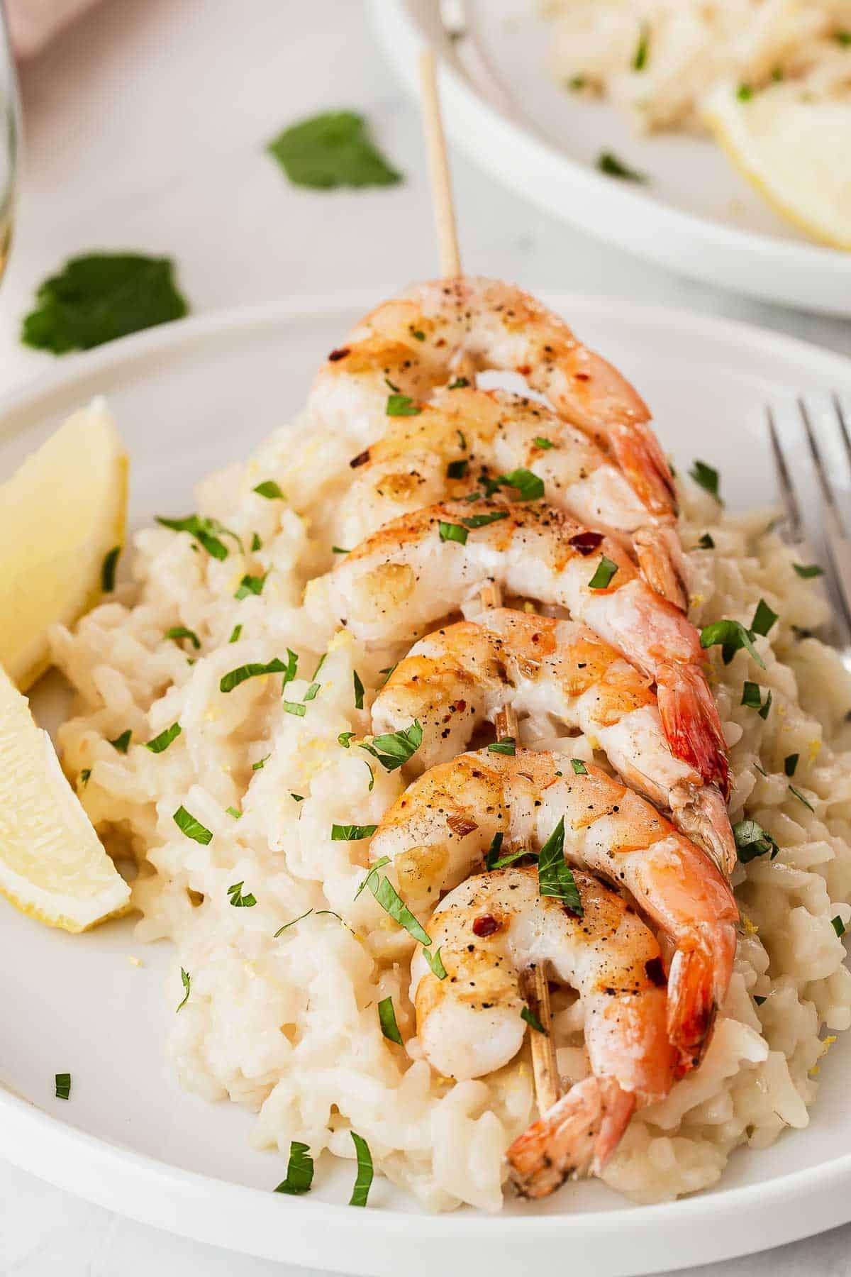 Primo piano di gamberi su risotto al limone con spicchi di limone.