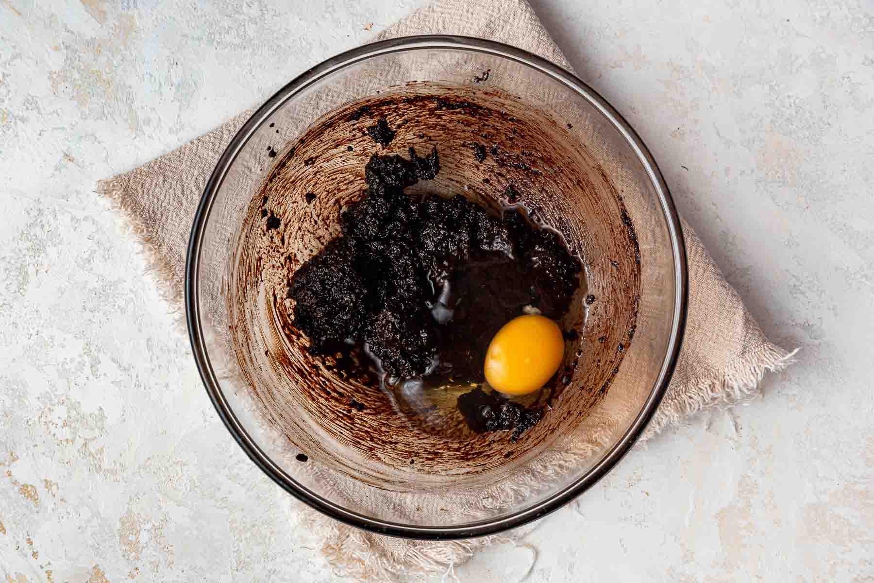 Uovo crudo che cade nell'impasto dei brownies in una ciotola di vetro trasparente.