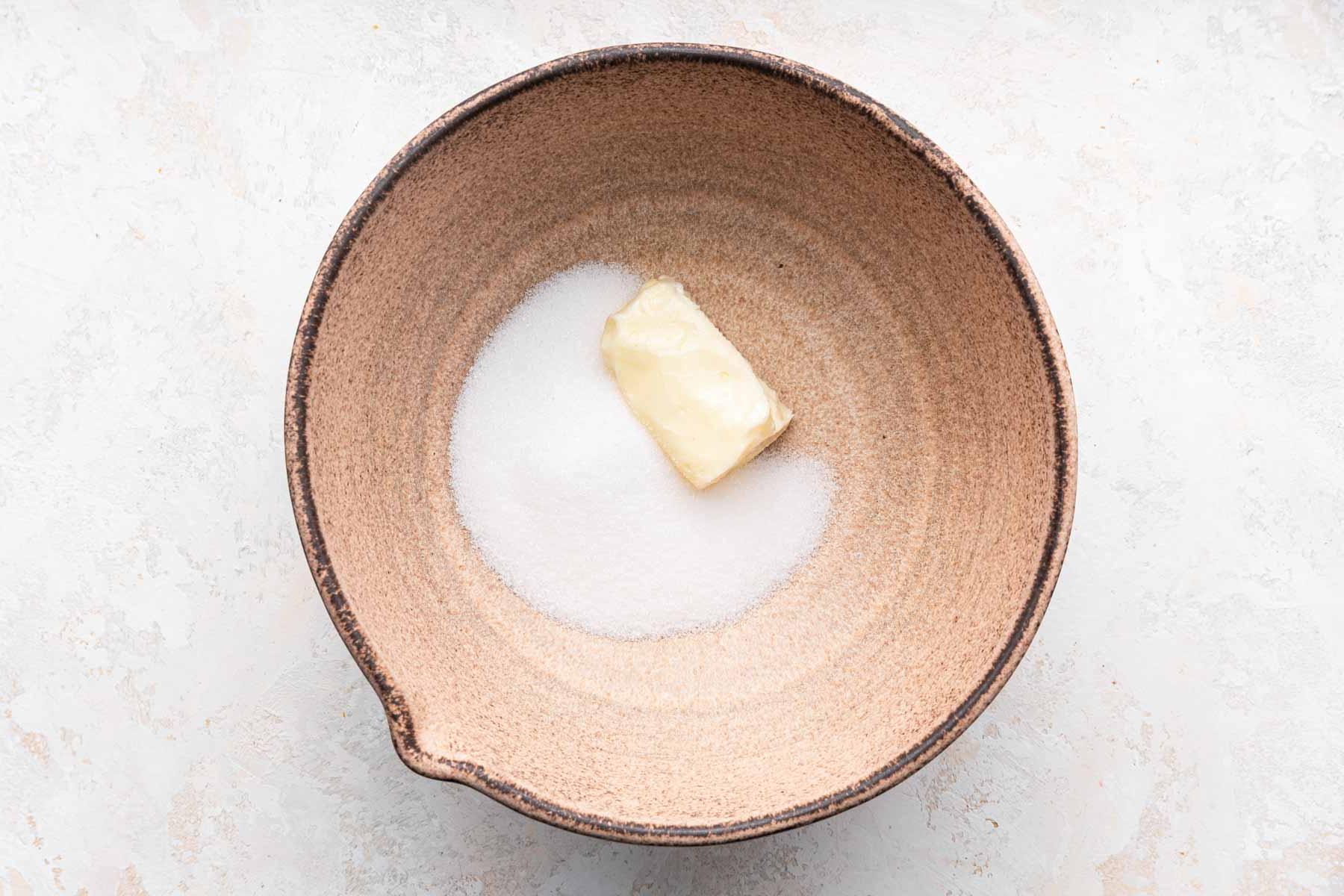 Brown bowl with half a stick of butter and granulated sugar.