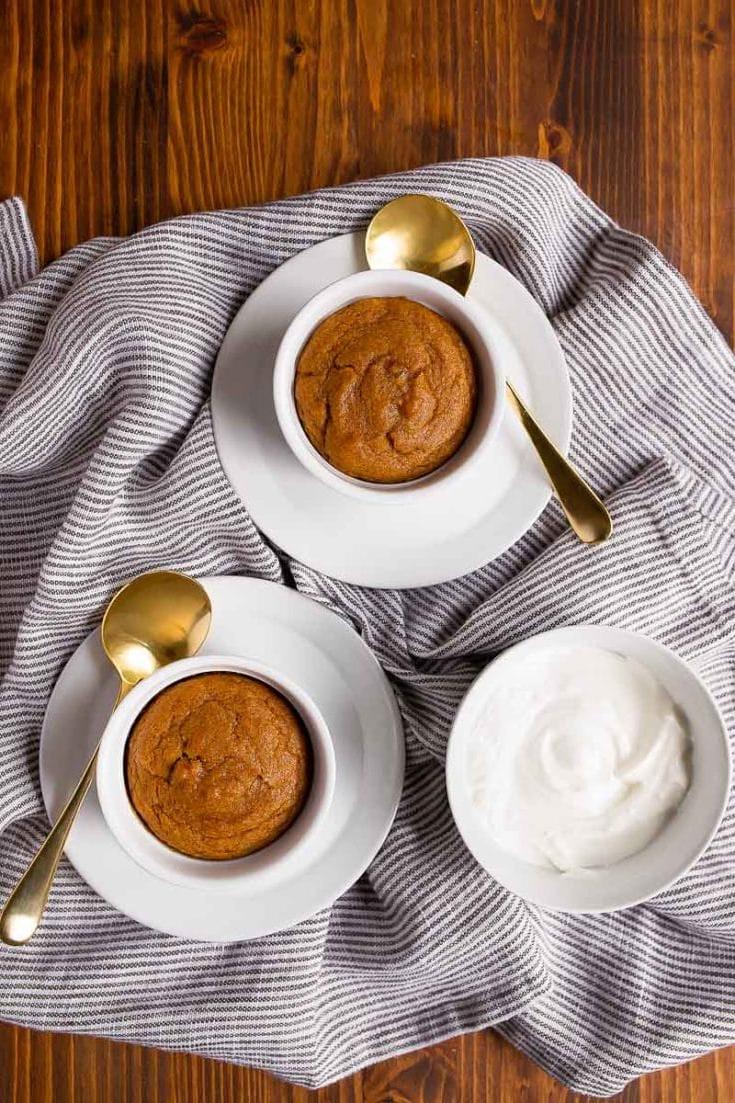 Un piatto di tortine di zucca in cocotte, guarnite con panna montata e spezie.