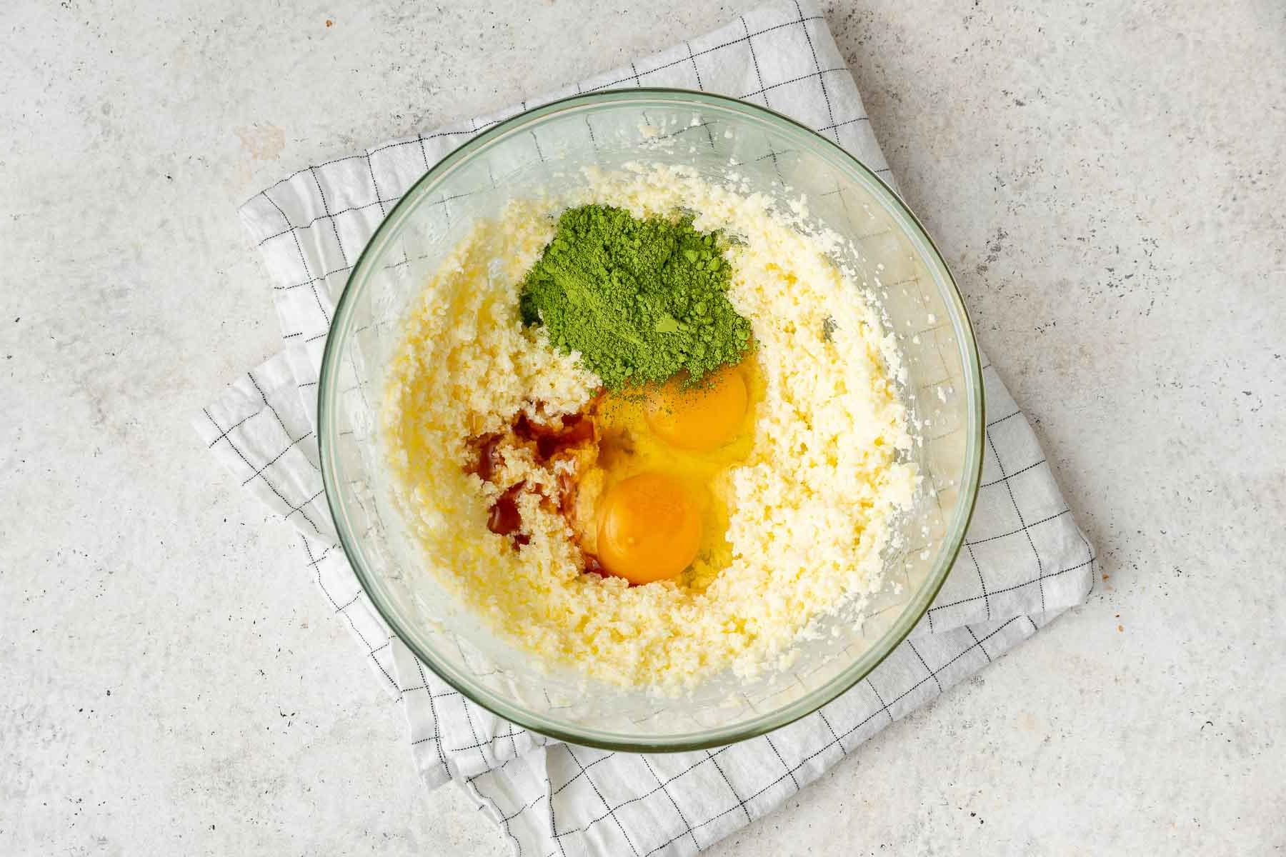 Torta al Matcha 6 Aggiungere uova, polvere di matcha e vaniglia all'impasto della torta in una ciotola di vetro trasparente.