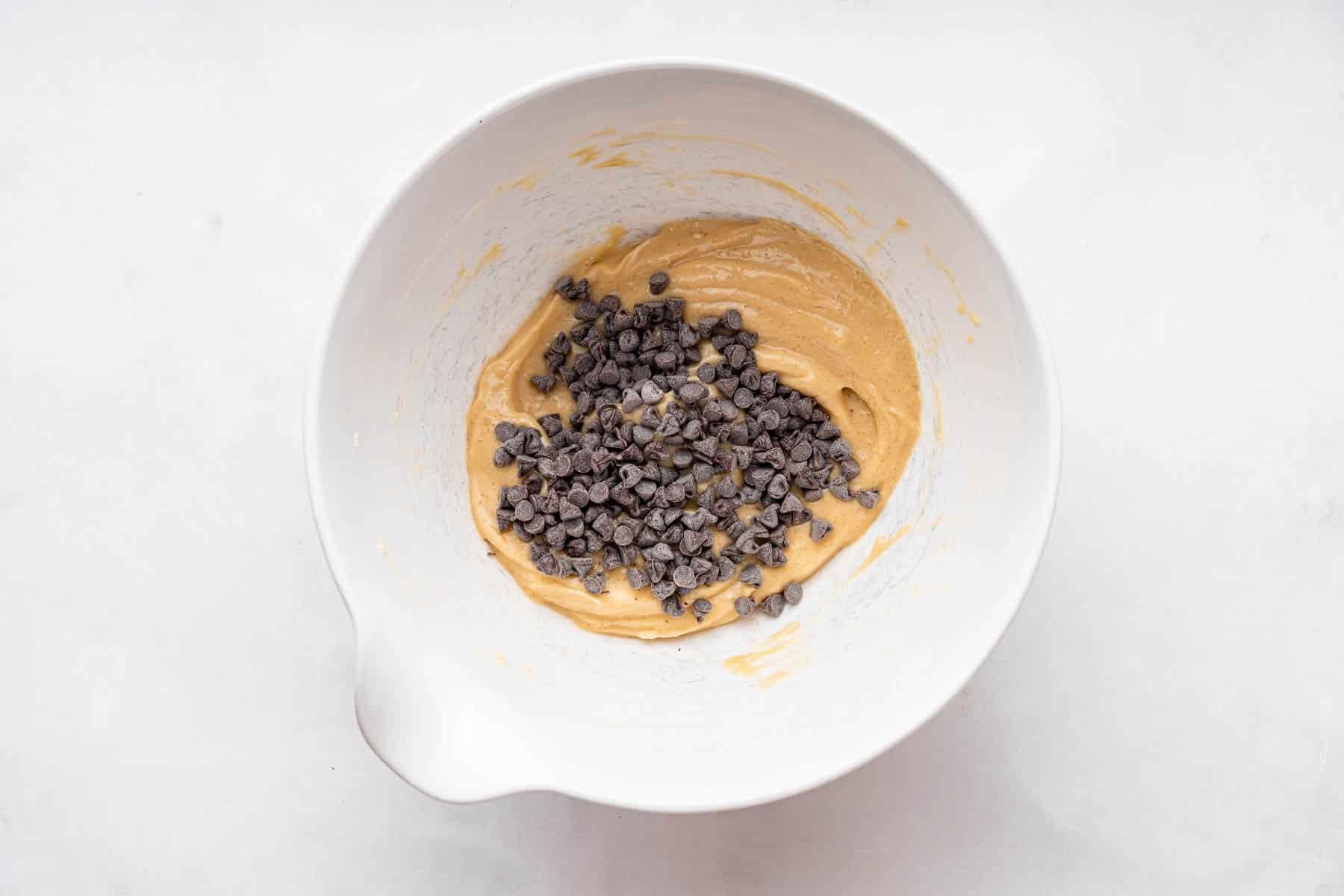 **Crema Impasto Biscotti Monoporzione** 6 Gocce di cioccolato sparse sull'impasto marrone del dessert in una ciotola bianca, pronte per essere incorporate.