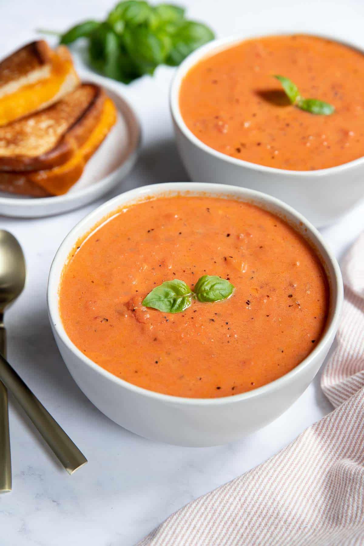 Due ciotole di zuppa di pomodoro con formaggio grigliato e basilico fresco.