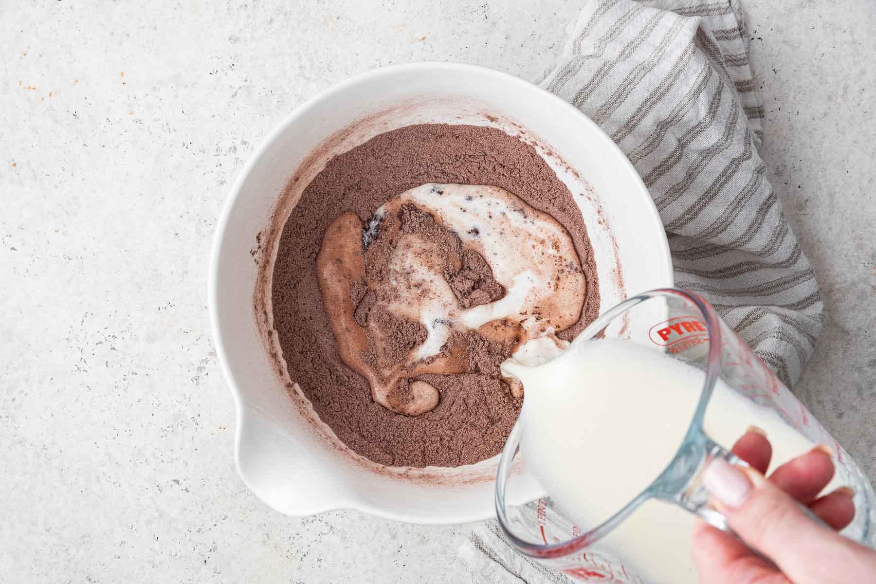Ricetta Torta al Cioccolato in Tazza 7 Versare il latte in una miscela di cacao in polvere in una ciotola bianca.