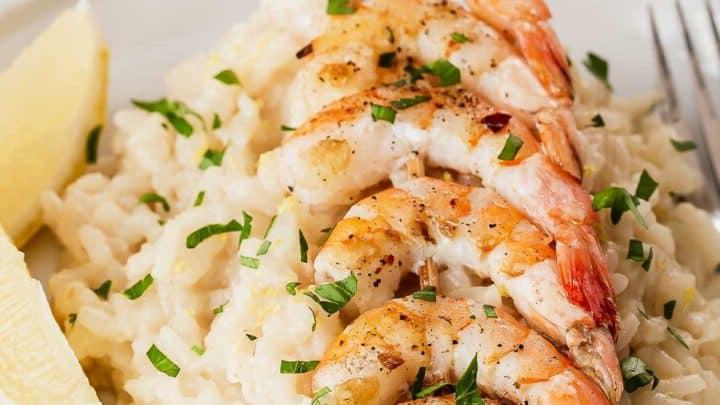 Primo piano di gamberi su risotto al limone con spicchi di limone.