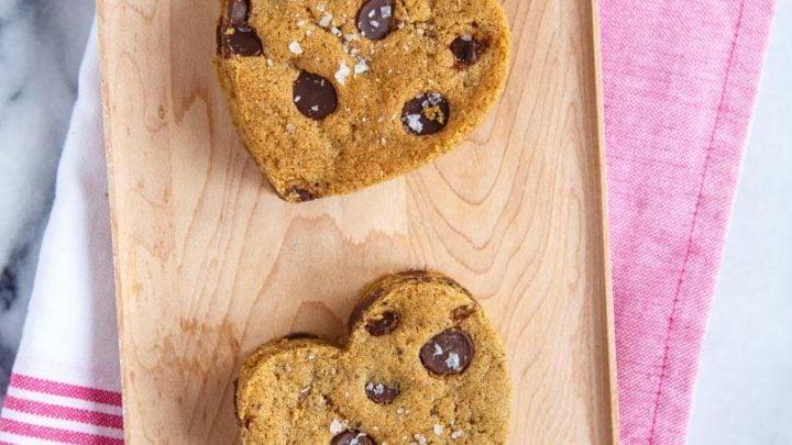 Biscotti Ritagliati con Gocce di Cioccolato 7 Due biscotti con gocce di cioccolato ritagliati a forma di cuore su un vassoio di legno.