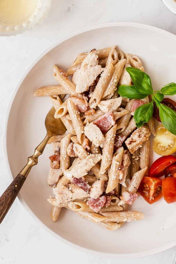 Un piatto di pasta con pollo e pancetta su una superficie di legno